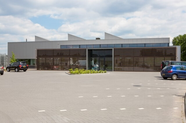 Modern kantoorgebouw met parkeerplaats op zonnige dag.