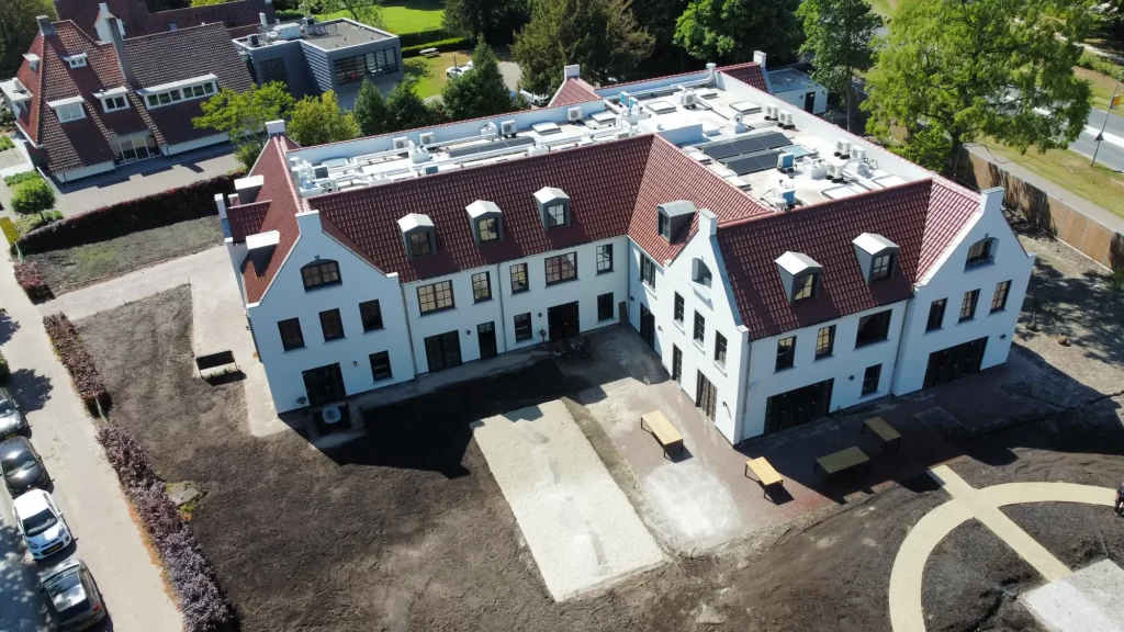 Luchtfoto wit gebouw met rode daken en parkeerplaats.