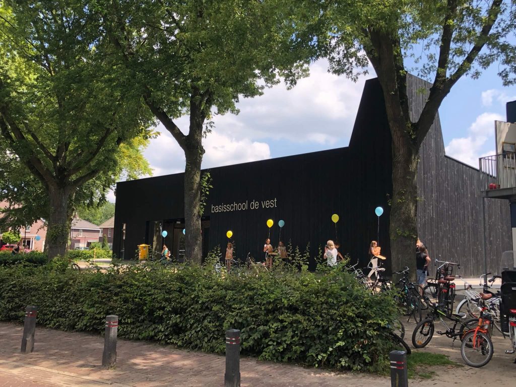 School met kinderen en ballonnen buiten gebouw.