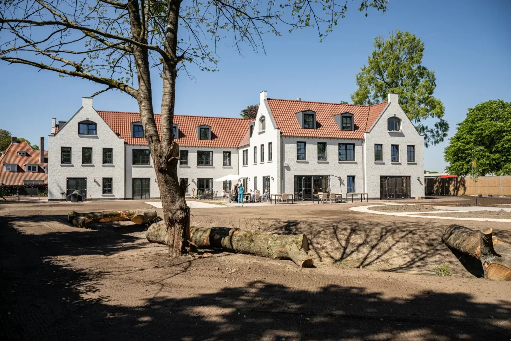 Groot wit huis met rode dakpannen, boom ervoor.