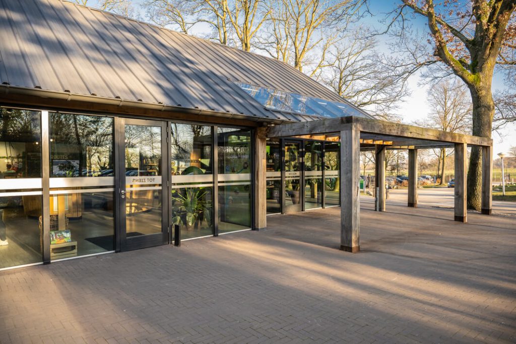 Ingang gebouw met glazen deuren en houten overkapping