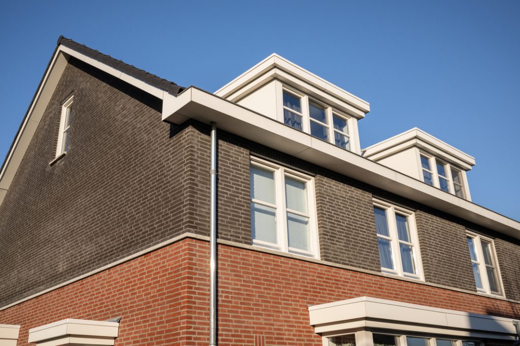 Moderne bakstenen woning met dakkapel en blauwe lucht.