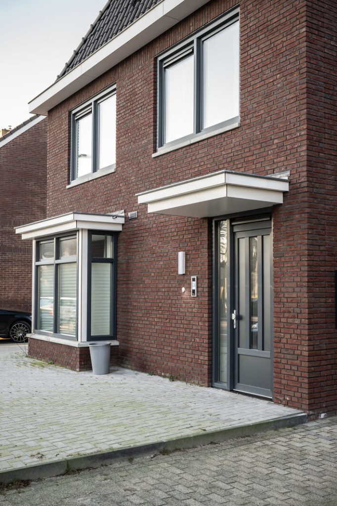 Voordeur van rood bakstenen huis met grote ramen.