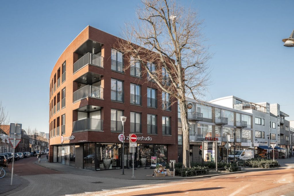 Modern bakstenen hoekgebouw met winkels en appartementen.