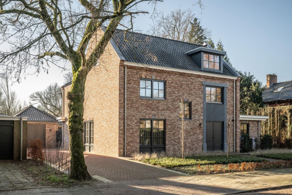 Bakstenen huis met oprit en grote ramen.