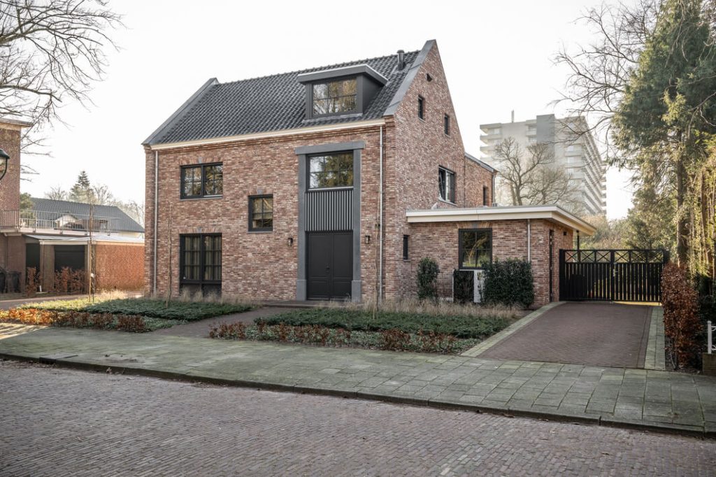 Roodbakstenen huis met tuin en oprit bij zonlicht.