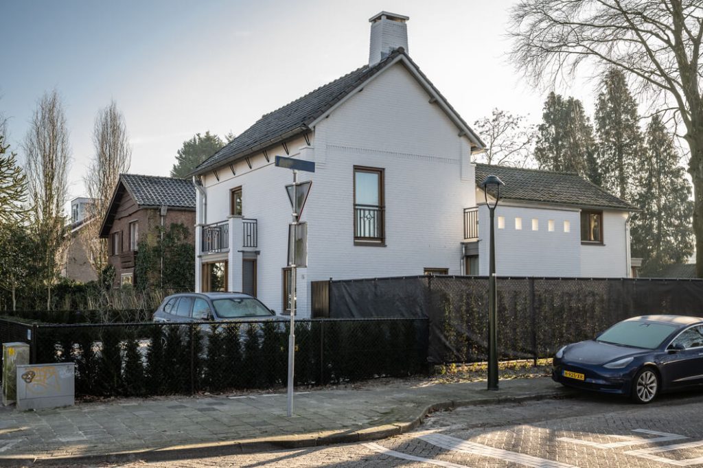 Wit huis in rustige woonwijk met auto's en tuin.