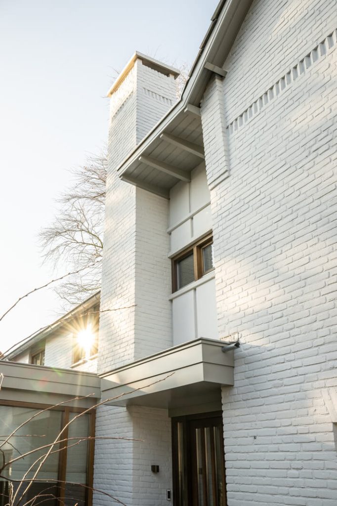 Witte bakstenen gevel met schoorsteen, zonlicht zichtbaar.