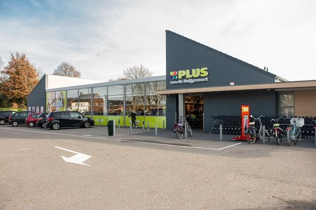 Buitenkant supermarkt met parkeerplaats en fietsenstalling.