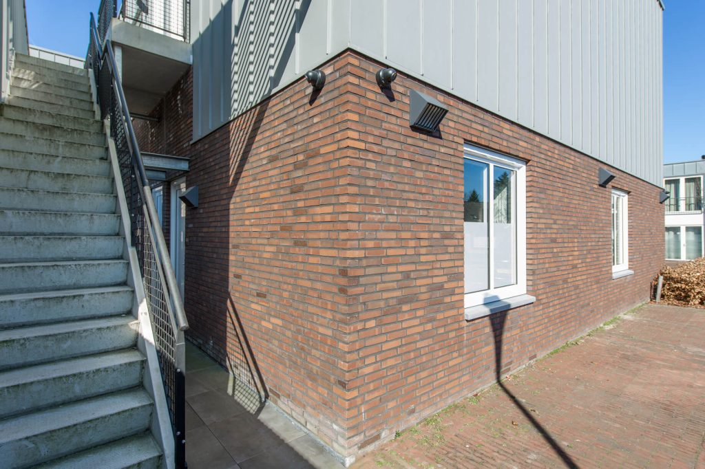 Bakstenen gebouw met buitentrap en schaduwen.