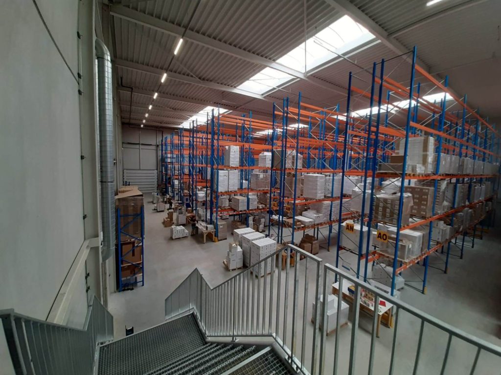 Grote opslagruimte met stellingen vol dozen en pallets.