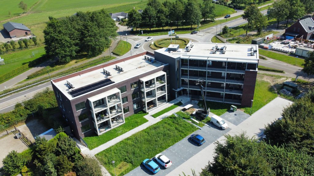 Luchtfoto modern gebouw met parkeerplaats en groen omgeving.