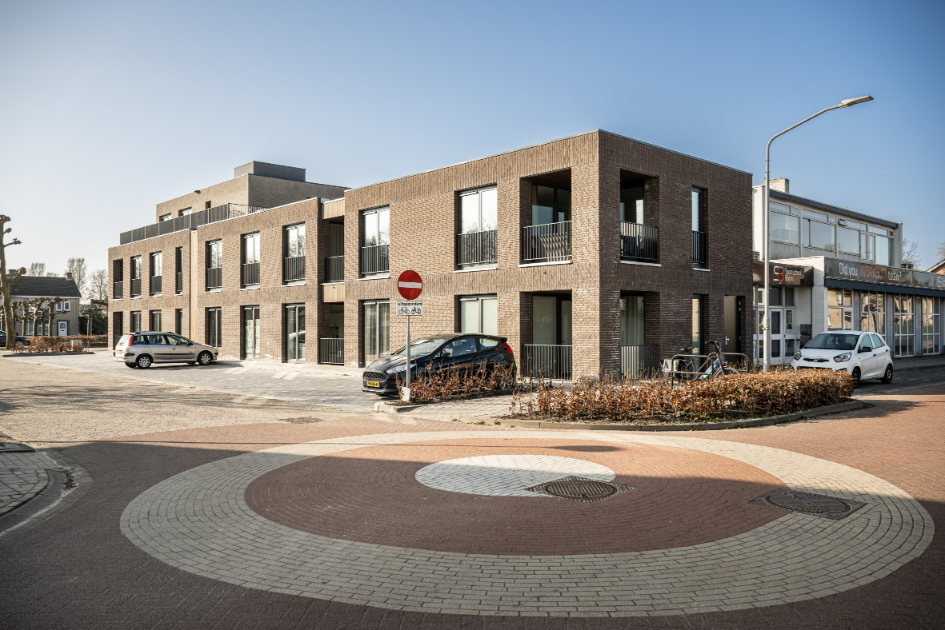 Modern appartementsgebouw met parkeerplaats op zonnige dag.