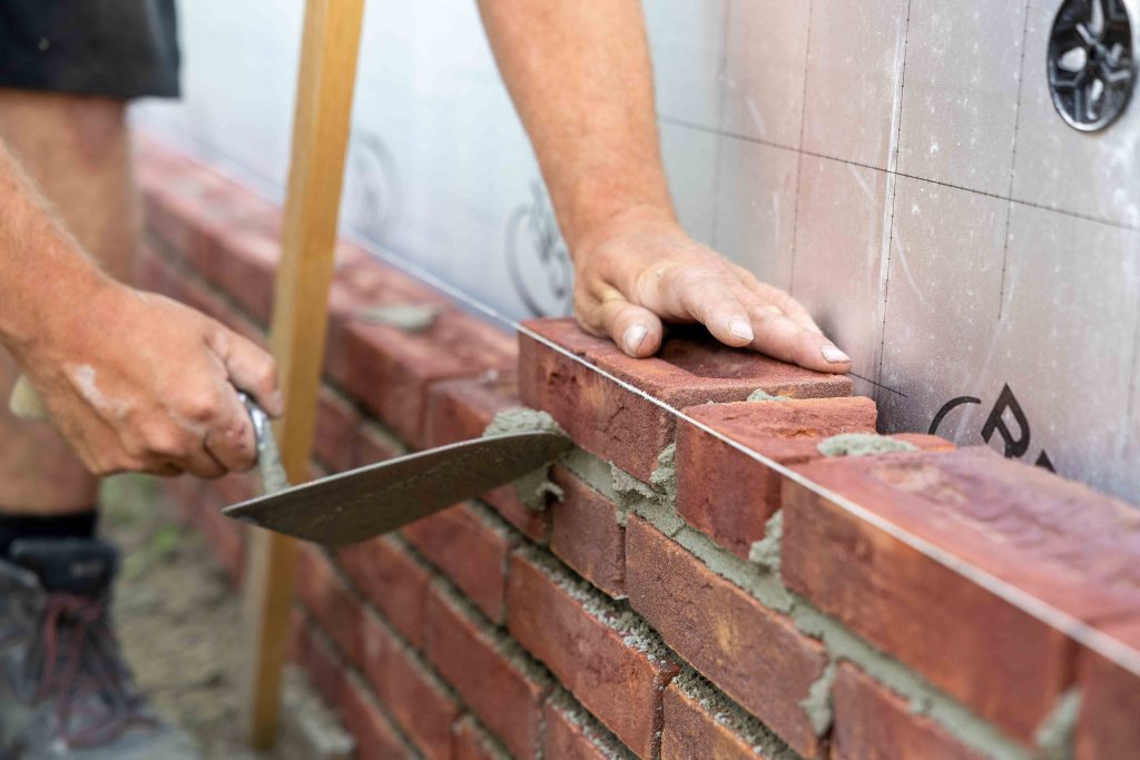 Metselaar bouwt rode bakstenen muur met troffel